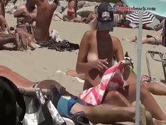 A gorgeous woman goes topless and gets a tan on a beach in the natural setting.